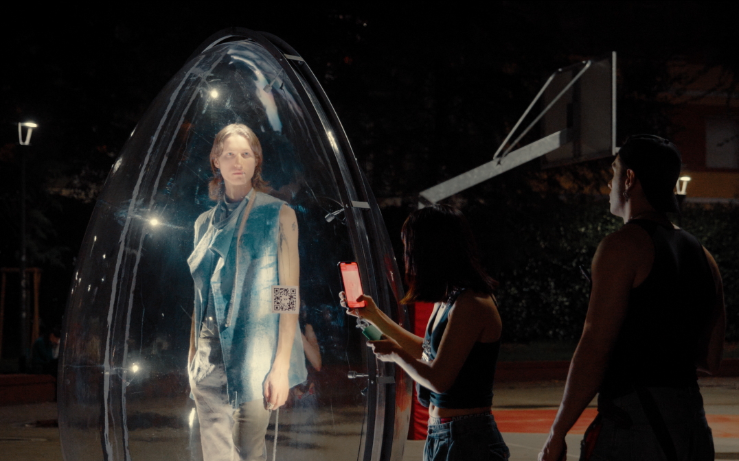 Person holding a phone to a QR code on a transparent egg with a model inside, in Diesel's Egg Hunt