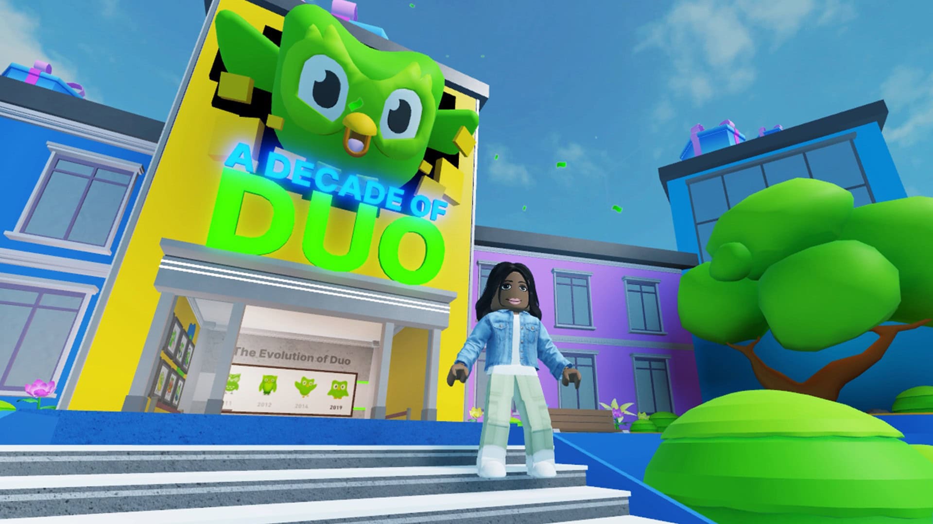 Duolingo Game Hub on Roblox: an avatar in a denim jacket stands on steps in front of a yellow building with a giant green Duo owl and a sign reading A Decade of Duo