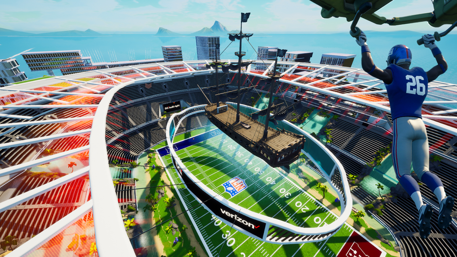 A Fortnite player in a blue number 26 football uniform glides down into Verizon's 5G Stadium, where a pirate ship hangs above an NFL field ringed by a track with a Verizon sign
