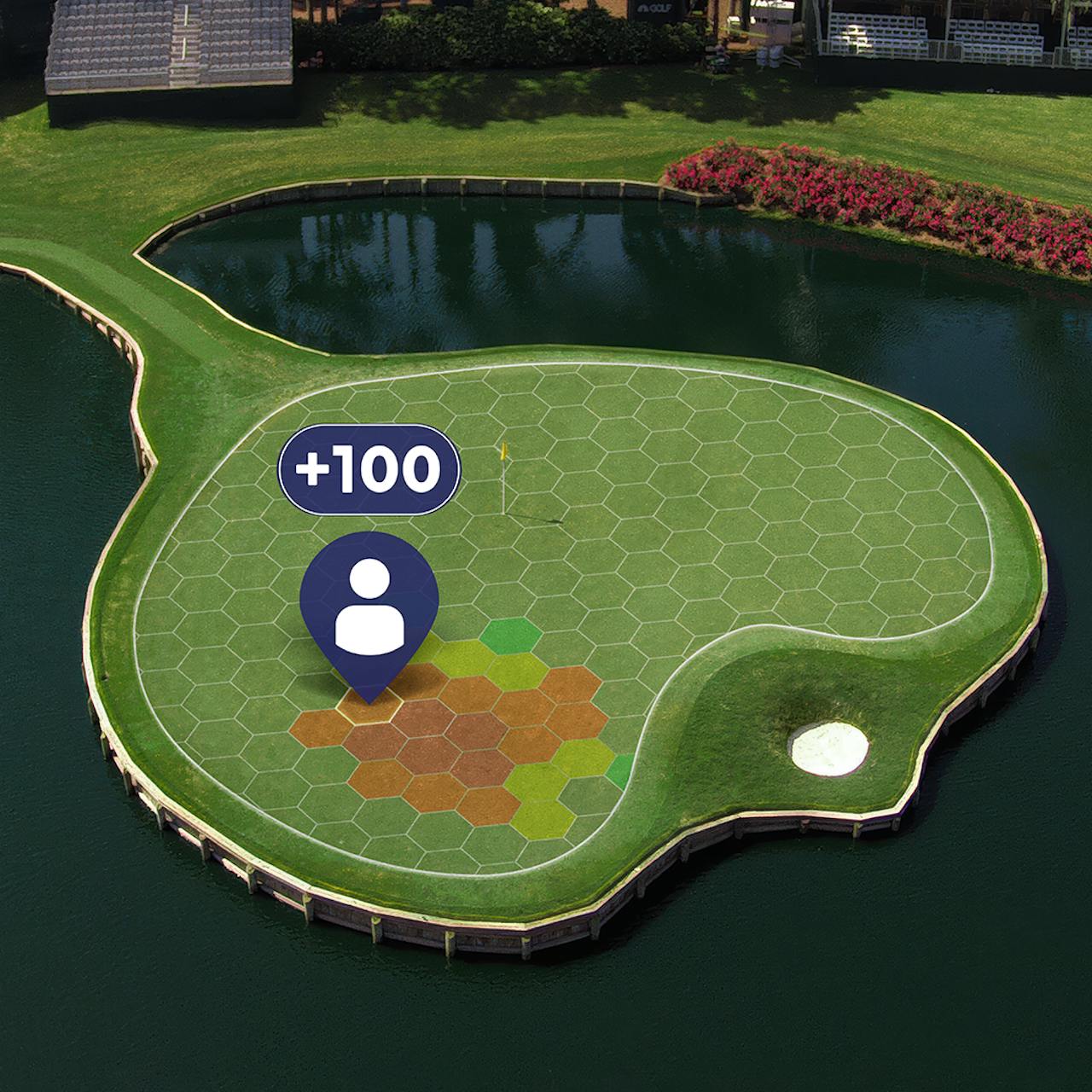 Game The Green by Comcast Business: an aerial view of an island green ringed by water under a hexagon grid, with a player's pin, a +100 points badge and hexes shaded from green to orange around the pick