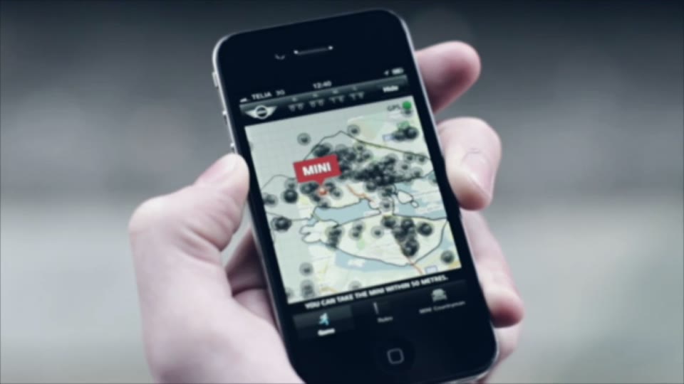 A hand holds an iPhone running MINI's Getaway Stockholm: a city map with a red MINI marker among dozens of dark markers and the line You can take the MINI within 50 metres