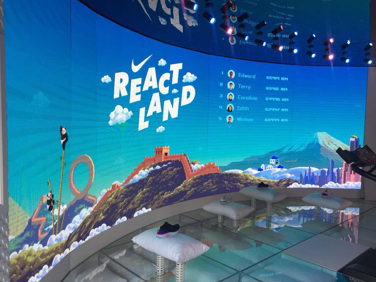 Nike Reactland installation: a curved screen with the React Land title, a pixel-art world with the Great Wall and pandas, and a leaderboard of players' distances in km, above trainers displayed on cushions