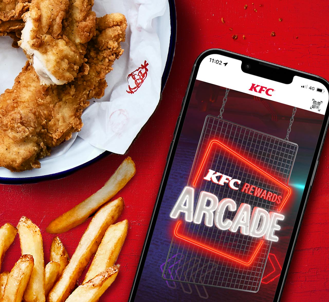 A phone showing the neon KFC Rewards Arcade screen in the KFC app, next to fried chicken and chips on a red table, Rewards Arcade by KFC