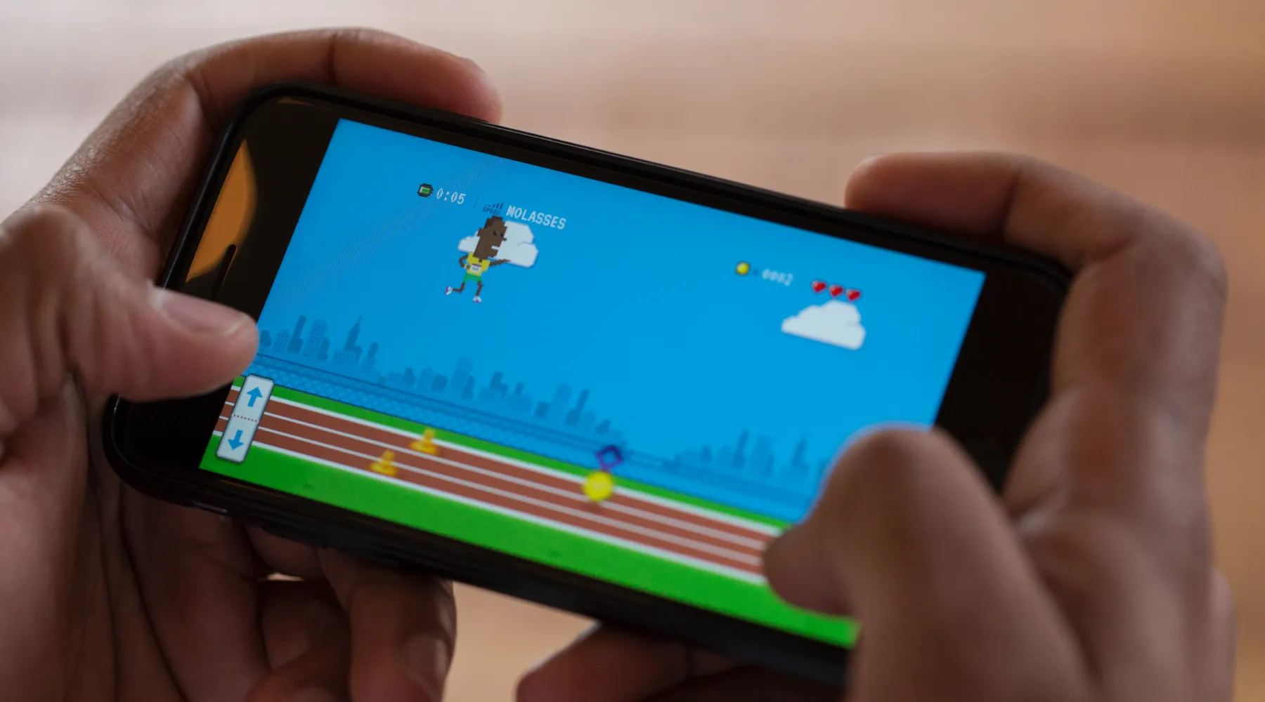 Run Puma Run on a phone held sideways: a pixel-art sprinter in a yellow and green kit leaps above a running track with cones and a gold medal on it, a timer, three hearts and up and down arrows on screen
