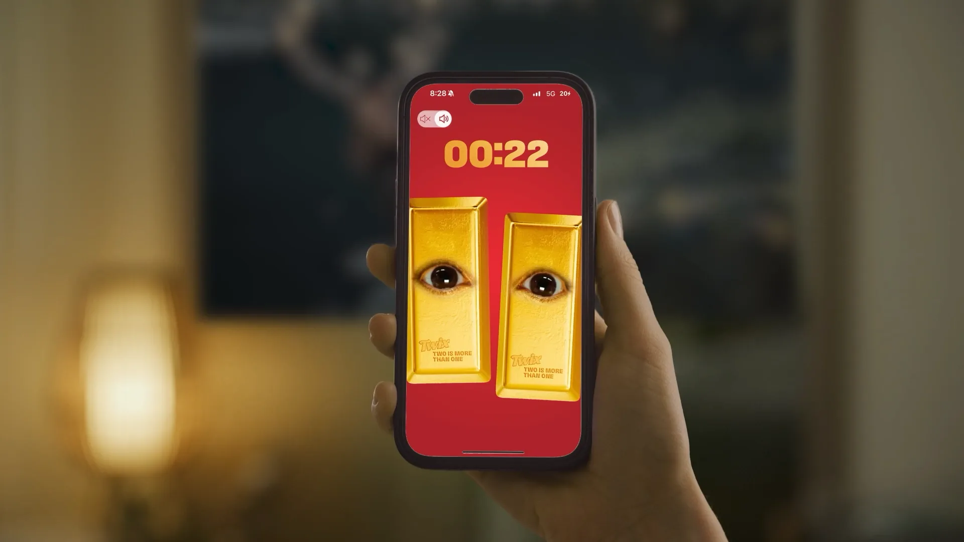 A phone held up shows Twix's Second Screen Staredown: two gold bars with human eyes under a timer.