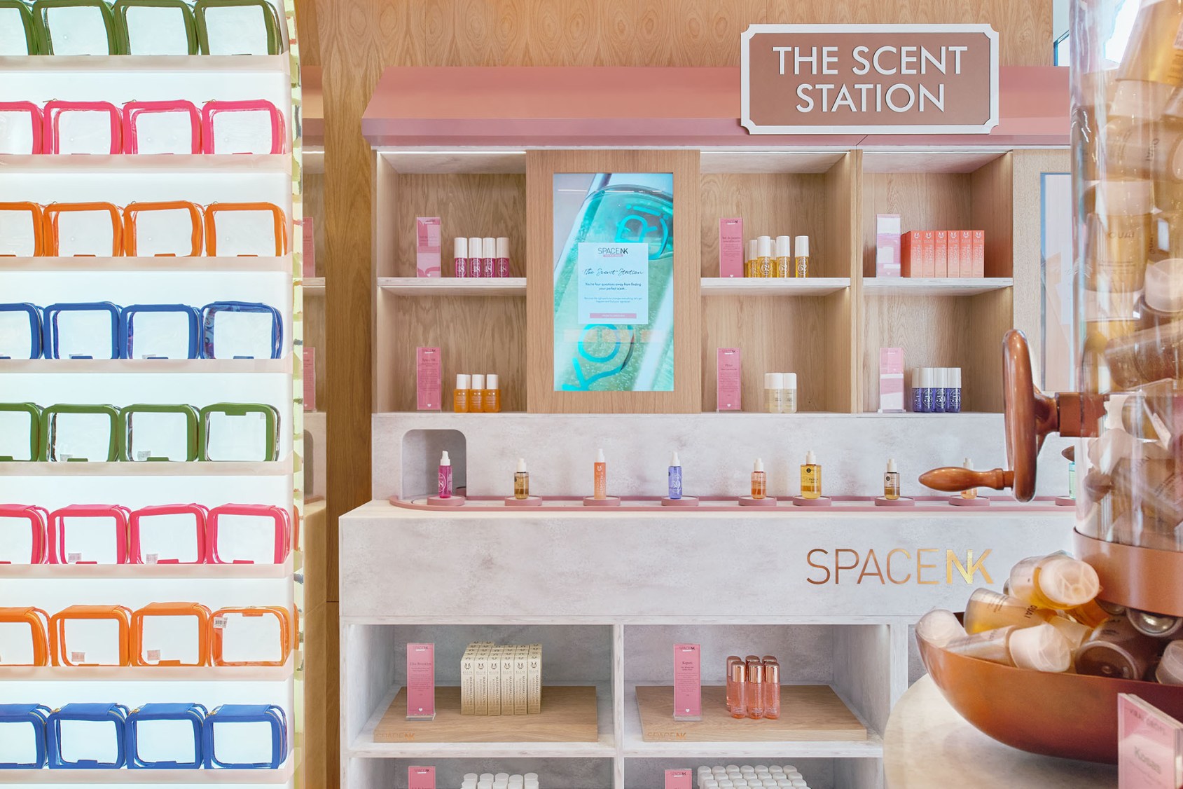 Space NK's Scent Station: a portrait screen set into wooden shelving shows the quiz start page, saying you're four questions away from finding your perfect scent, above a counter lined with fragrance testers