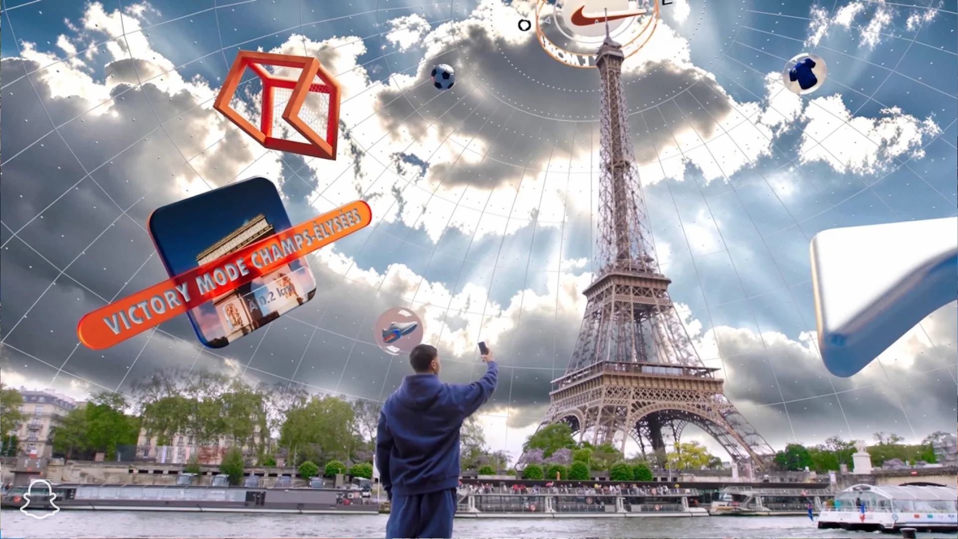 Nike Victory Mode Snapchat lens in Paris: a young man by the Seine holds up his phone towards the Eiffel Tower while a grid dome, a Nike compass, a football goal and a Victory Mode Champs-Élysées marker float in the sky