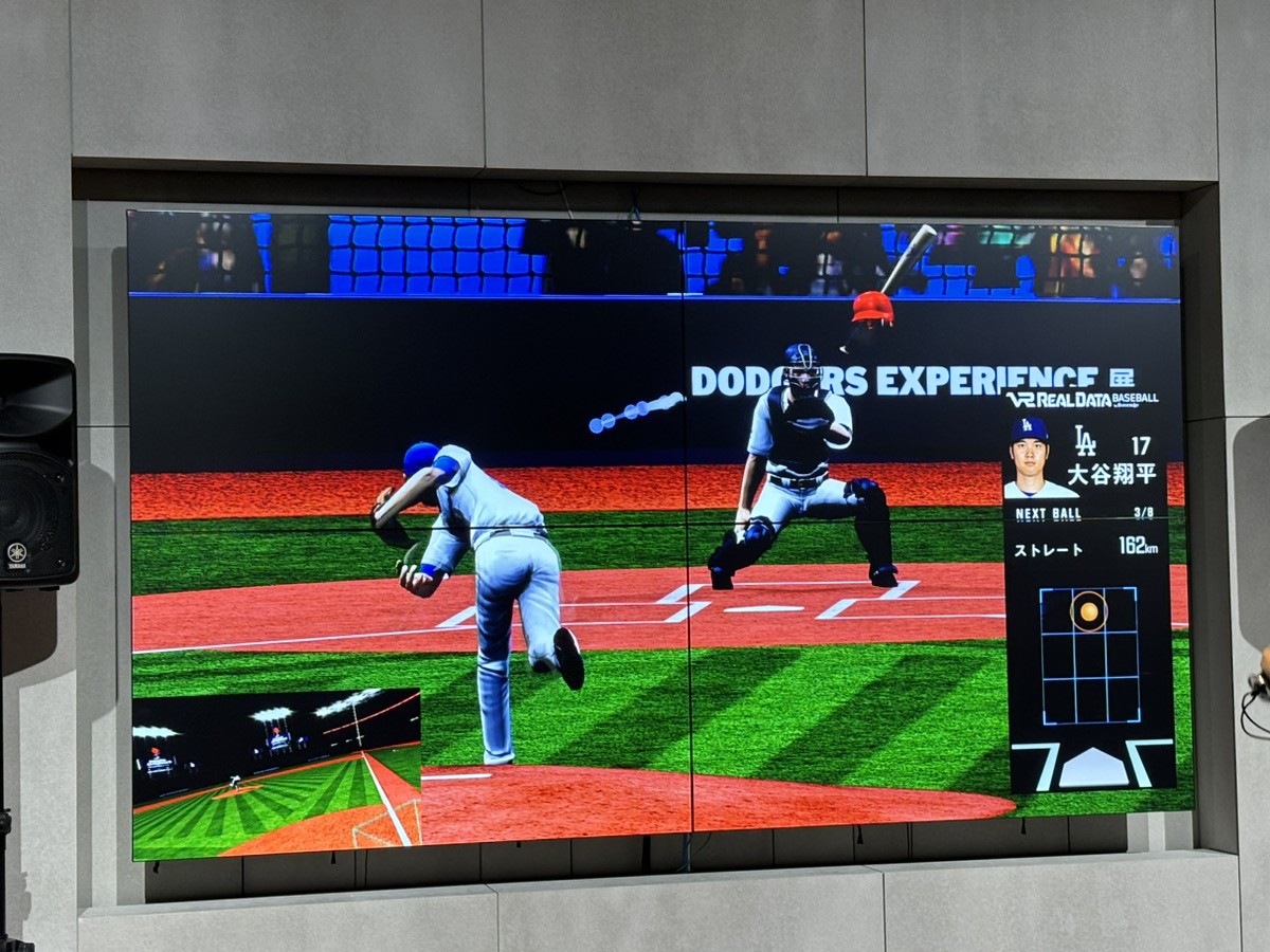 VR Real Data Baseball for the Dodgers on a wall screen at the exhibition: a batter swings at home plate in a virtual stadium as the catcher waits, beside a panel showing Shohei Ohtani's next pitch, a 162 km/h fastball, over a strike-zone grid